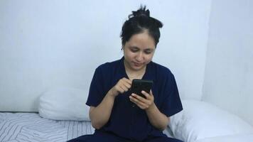 Smiling young woman using mobile phone while sitting in bed at home video
