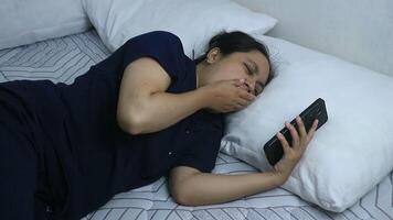 Asian woman using smart phone and yawning while lying on bed at home. Technology concept. video
