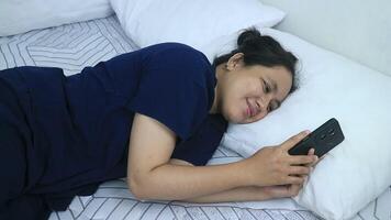 Smiling young woman using mobile phone while lying in bed at home video