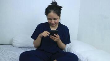 Smiling young woman using mobile phone while sitting in bed at home video