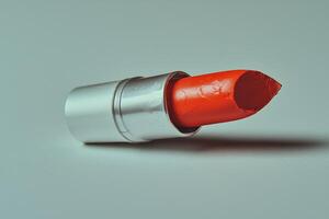 broken lipstick bullet rests on its side showcasing its bold red hue and creamy texture. pristine white background highlights rich pigment and details of broken surface photo