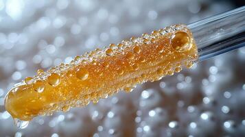 Close up view of clear lip gloss tube gold gloss and small bubbles catching light. applicator is pulled out showcasing product's texture and shimmer photo