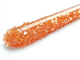close up view reveals lip gloss applicator dipped in rich rose gold gloss glossy droplet hanging from tip against clean white background photo