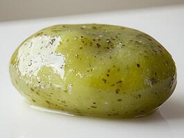 single pickled cucumber is captured in vivid detail showcasing its bumpy texture and bright green hue. glistening brine enhances its fresh appearance against plain backdrop photo