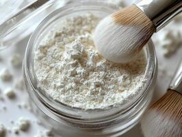Soft light enhances translucent loose powder in clear jar lid slightly open and fluffy brush resting beside it on clean white background photo