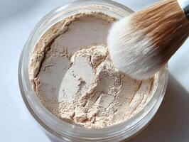 Translucent loose powder rests in clear jar lid slightly open beside fluffy brush on light backdrop showcasing its fine texture and soft lighting photo