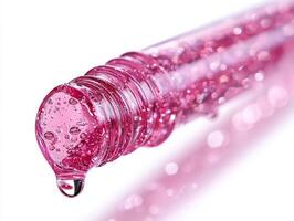 Clear pink lip gloss drips off rounded applicator tip creating eye catching effect. smooth texture and shine are highlighted against white background enhancing its vibrant color photo