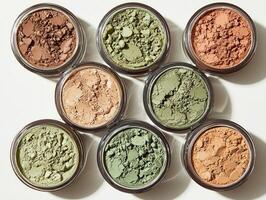 Cream eyeshadow pots are arranged showcase shades of champagne olive green and bronze. creamy textures reflect soft light against clean simple background photo