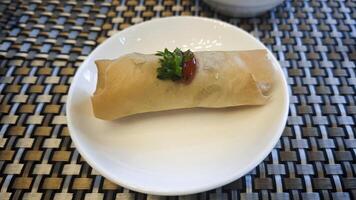 Crispy Spring Roll Garnished with Parsley and Chili Sauce on White Plate with Woven Table Mat Background photo