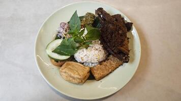Traditional Indonesian Kecombrang Rice with Fried Spiced Duck Tempeh Tofu Assorted Sambals Fresh Basil and Cucumber Served on a Light Green Plate on Neutral Table Background photo