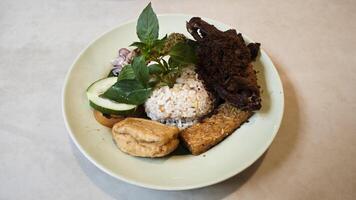 Traditional Indonesian Kecombrang Rice with Fried Spiced Duck Tempeh Tofu Assorted Sambals Fresh Basil and Cucumber Served on a Light Green Plate. photo