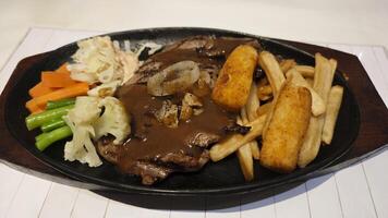 Grilled beef steak served with creamy brown gravy crispy potato wedges French fries and sauteed vegetables on a black sizzling plate creating a delicious hearty meal presentation. photo