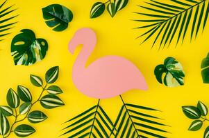 Trendy summer pattern composition made of tropical green leaves on yellow background with pink flamingo paper card note copy space. Minimal creative summer concept. Nature backdrop idea. Flat lay. photo