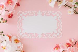 Beautiful orchid flower on light pastel pink background with white paper card note copy space. Minimal spring and summer concept. Flowers aesthetic. Flat lay, top of view. photo