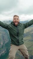 Joyful Male Adventurer Celebrating Amidst Majestic Mountain Landscape with Overcast Sky Showcasing Outdoor Enthusiasm and Authentic Exploration Spirit Captured in Vertical Portrait Format photo