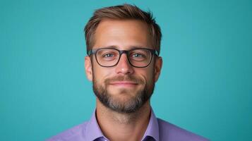Portrait of a man with glasses and beard wearing a purple shirt. Studio shot against a teal background. photo