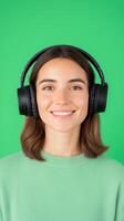 Smiling Woman Holding Black Headphones Against Vibrant Green Background for Modern Music Enthusiasts and Creative Content Creators in Vertical Orientation photo