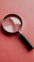 Metallic magnifying glass on vibrant red background, highlighting elegance and functionality Vertical Mobile Wallpaper photo