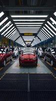 Red car at forefront on assembly line, highlighting efficient automotive production process. Vertical Mobile Wallpaper photo