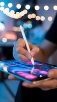 Hands holding stylus work on vibrant digital tablet with blue and pink graphics. Vertical Mobile Wallpaper photo