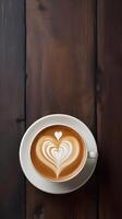 Heart-shaped latte art fills the coffee cup, placed on a dark wooden surface, with steam and texture creating room for a Valentine message. photo