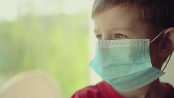 Boy and his teddy bear both in protective medical masks sits on windowsill and looks out window 04 video