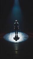 Lone figure stands in spotlight on dark stage, casting shadow, creating dramatic atmosphere Vertical Mobile Wallpaper photo