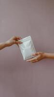 Hands exchanging a rectangular white pouch, minimalist composition of transfer gesture Vertical Mobile Wallpaper photo