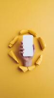 A vibrant yellow background with a hand breaking through, holding a blank object Vertical Mobile Wallpaper photo