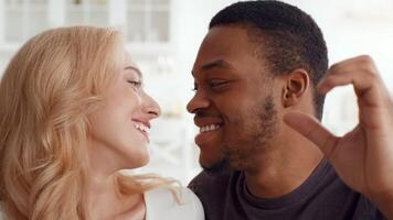un' birazziale coppia felicemente le forme un' cuore forma con loro mani, sorridente affettuosamente a ogni altro nel loro accogliente casa. il caldo ambiente cattura loro legame e amore perfettamente. video