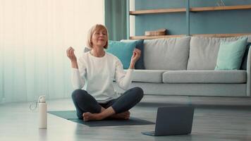 A senior woman practices yoga in her living room, sitting cross-legged on a mat. She is focused and calm, enjoying the moment of mindfulness while connecting with her body. video
