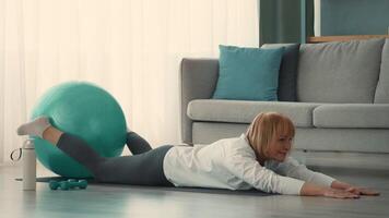 A senior woman engages in a workout routine at home, balancing on an exercise ball with arms extended. She focuses on her fitness and well-being in a bright, cozy environment. video
