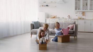 Two girls and woman enjoy playful activities in a bright, modern living room while exploring cardboard boxes. Laughter fills the air as they share simple moments together. video