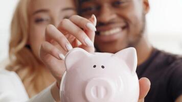 A biracial couple is sharing a joyful moment at home while saving money in a piggy bank. Their love and affection shine as they bond over this financial goal in a cozy setting. video