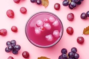 Glass of grape juice with ice cubes and fresh grapes on pink background photo