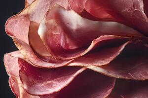Smoked ham prosciutto crudo forming a flower shape on black background photo