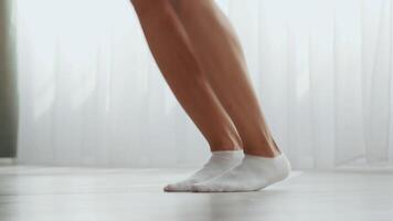 A millennial woman engages in a fitness routine at home, showcasing her athletic ability. She emphasizes leg strength and flexibility while wearing comfortable socks on a wooden floor. video