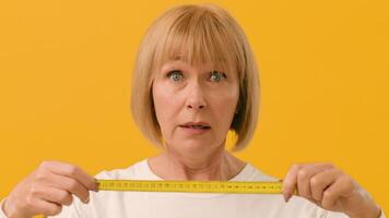 A woman focuses intently on measuring an object, using a yellow tape measure in front of a bright yellow background, showcasing her concentration and precision in task completion. video