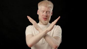 A young man with albino traits shows a clear expression of disapproval. His white hair and light skin contrast sharply with the dark backdrop, creating a striking visual impact. video