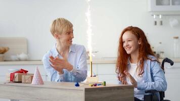 A teenage girl in a wheelchair and a smiling adult celebrate a birthday at home. They enjoy colorful decorations, presents, and a sparkling candle on a cake, filled with joy and laughter. video