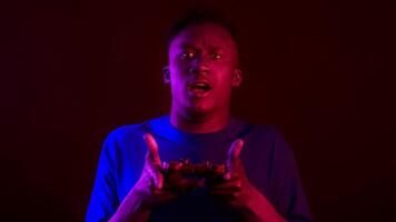 A handsome millennial man intensely focuses on gaming while holding a controller. The vibrant neon lights create a futuristic atmosphere around him, enhancing the gaming experience. video
