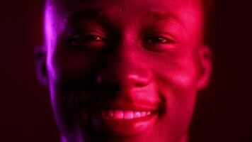 A cool, millennial African American man smiles confidently against a vibrant neon background. The setting highlights modern aesthetics combining futurism with trendy hipster vibes. video
