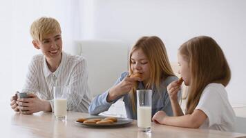 Three family members gather around a table, enjoying cookies and milk together. One child happily bites into a cookie while the others watch, creating a delightful moment. video