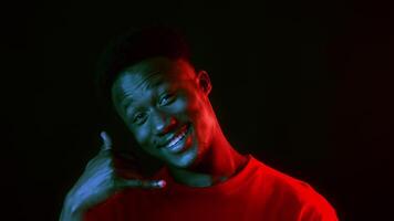 A confident man stands in front of a dark backdrop, illuminated by vibrant neon colors. His stylish look and smile convey a modern, hip vibe, capturing the essence of youthful energy. video