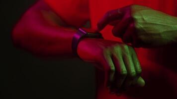 A man with an impressive look is inspecting his smartwatch while illuminated by vibrant neon colors. The futuristic vibe adds to the cool atmosphere of the moment. video