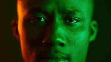 A handsome millennial man is staring directly at the camera with a strong expression. He is illuminated by vibrant green neon colors, emphasizing his features in a trendy, modern setting. video
