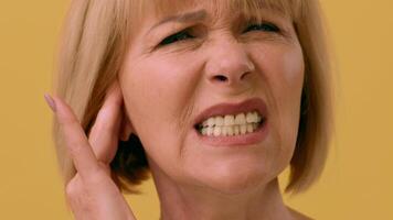 A woman is grimacing while holding her ear, suggesting discomfort or pain. The bright yellow background enhances the emotional intensity of her expression, indicating distress. video