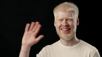 A young man with white hair and pale skin is smiling, showcasing his unique features. He exudes warmth and confidence while dressed casually, captured in a simple environment, copy space video