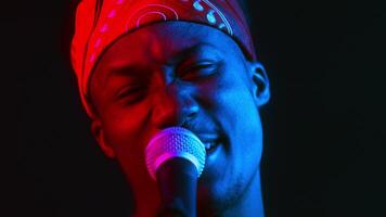 A stylish African American man with a confident expression sings into a microphone. The vibrant neon lighting creates a striking contrast, enhancing his cool, hipster vibe. video