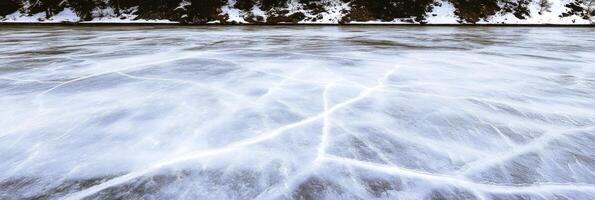 Frozen lake surface with natural ice cracks and snowy shoreline in winter landscape photo